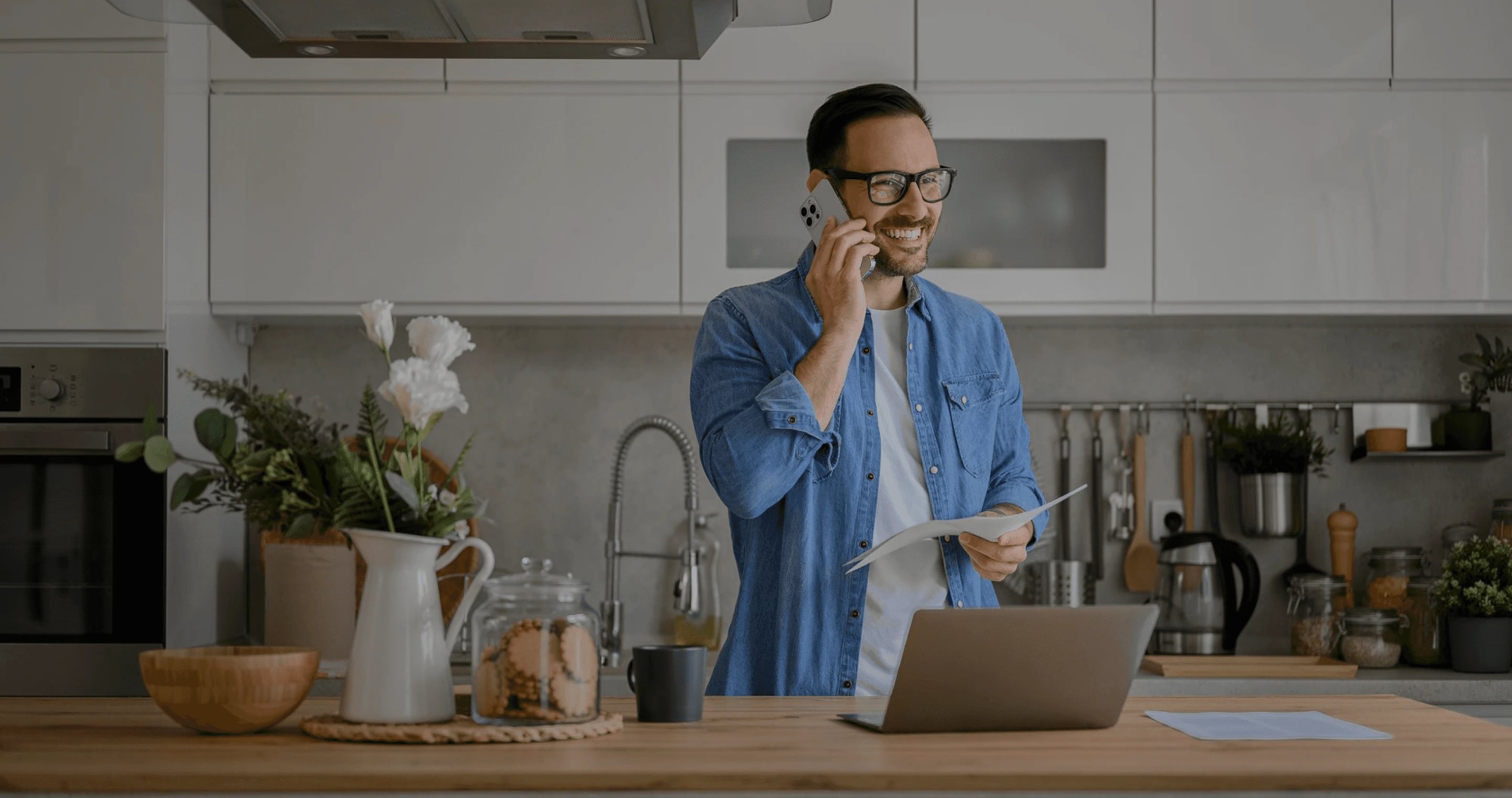 Emprendedor conversando por teléfono y revisando documentos en su cocina